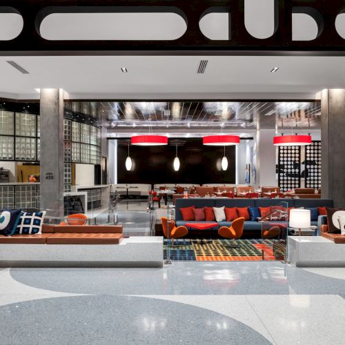 A modern lounge area with colorful couches, patterned cushions, and red circular light fixtures in a stylish space.