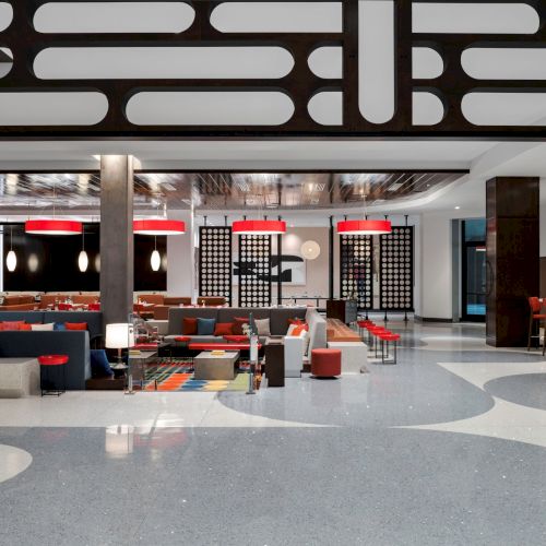 A modern restaurant interior with stylish furniture, red light fixtures, and a patterned floor design. The space has an open and inviting layout.