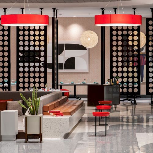 A modern lounge area with stylish seating, red accents, decorative partitions, and contemporary lighting and artwork.