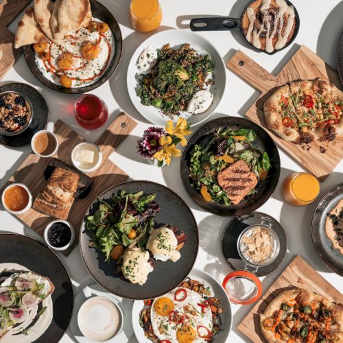 The image shows a variety of dishes, including salads, meats, breads, and drinks arranged on a table, suggesting a diverse meal spread.