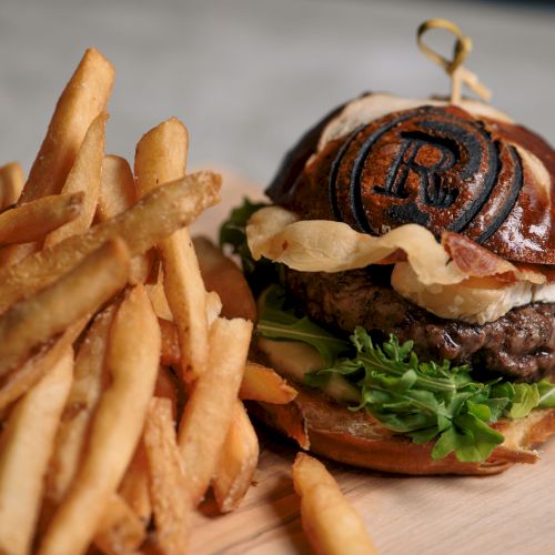 A burger with lettuce, cheese, and a branded bun alongside a serving of fries on a wooden board.