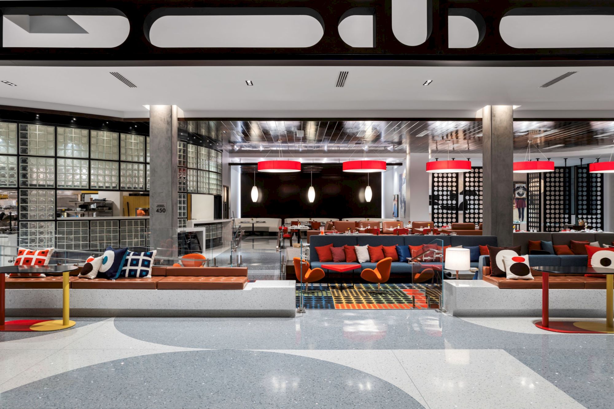 A modern lobby with colorful seating, geometric patterns, and red ceiling lights, featuring a stylish, open design and polished floors.